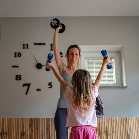 Young mother working out at home lifting weights with her toddler daughter exercising with her.の写真素材