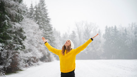 Young woman in bright yellow sweater standing mindfully with her arms spread in the middle of white...