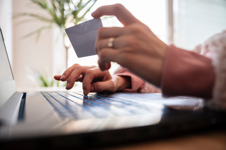 Low angle closeup view of female hands holding a credit card paying online on laptop computer. Conceptual image of online shopping or course purchasing.の写真素材
