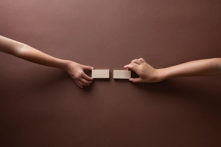 Hands of two children placing blank wooden pegs or tiles on a brown background. Top view.の写真素材