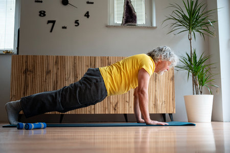 Side view of an active senior man in bright yellow shirt exercising at home making a plank position. Strength and core body workout for active retirement.の写真素材