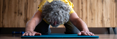 Wide view image of an active senior man taking care of his health in retirement. Exercising on a mat stretching in child pose while doing yoga or pilates.の写真素材