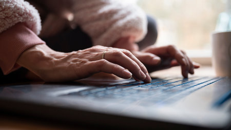 Low angle closeup view of female hands typing on laptop computer keyboard placed on the ground.の写真素材