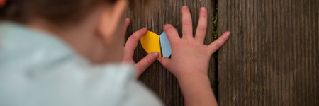 Overhead view of a child making a heart shaped paper in the colors of the Ukrainian flag. Conceptual of peace and safety for Ukraine. Wide view image.の写真素材
