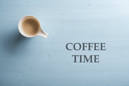 Top view of cup of fresh coffee placed over a simple plain light blue wooden background. Coffee time sign written next to it with black capital letters.の写真素材