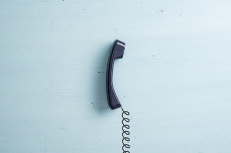 Black landline telephone receiver with a hand drawn cord attached to it placed over simple light blue wooden background. With plenty of copy space.の写真素材