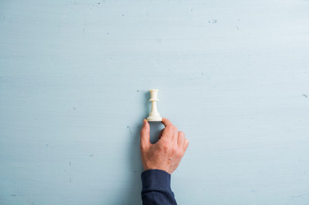 Male hand placing white king chess figure on a plain simple light blue wooden background. With plenty of copy space.の写真素材
