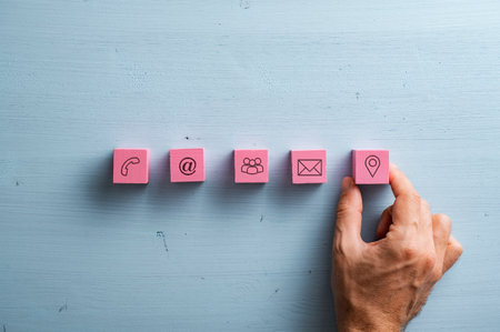 Male hand placing five pink wooden blocks with contact and communication icons on them over simple light blue wooden background.の写真素材