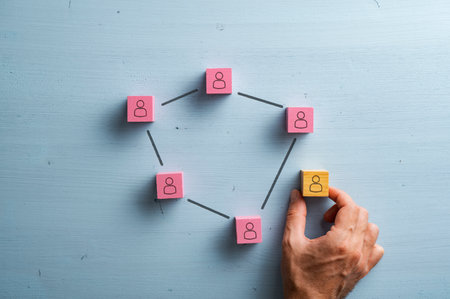 Pink wooden blocks wit a person icon on them connected by lines. Male hand placing another one next to the connected team in a conceptual image of social network connection. Over blue wooden background.の写真素材
