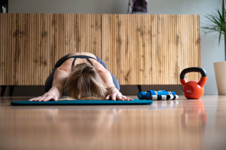 Low angle front view of a woman stretching in child pose after a home workout or pilates routine. On an exercise mat in domestic living room.の写真素材
