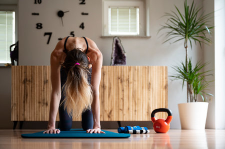 Front view of a slim fit young woman practicing yoga or pilates routine making a cat stretch exercise. On a workout mat in domestic living room.の写真素材