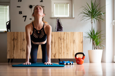 Young woman in sportswear stretching while arching her back. On a mat in domestic living room.の写真素材
