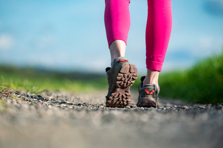 Low angle view of hiking shoe sole while walking on gravel trail. Of a woman in pink legging active outside.の写真素材