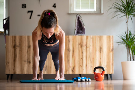 Low angle front view of a fit young woman holding a plank position while working out at home on a mat in domestic living room.の写真素材