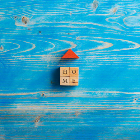 Top view of a house made of wooden blocks with a red roof and a Home sign on it. Over textured wooden background.の写真素材