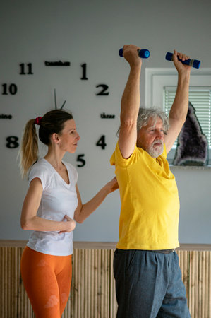 Professional physiotherapist working with a senior man teaching him how to workout properly with dumbbells to keep active, strong and healthy.の写真素材