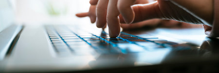 Low angle closeup view of female hands typing on laptop computer keyboard lit by bright light coming from the background. Wide view image.の写真素材