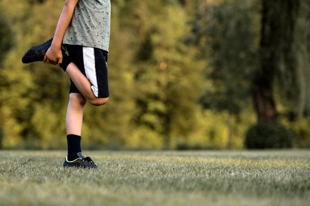 Child warming up before soccer practice stretching his leg holding his foot. On a green grass playing field.の写真素材
