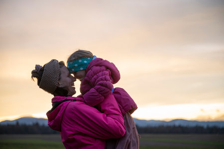 Joyful young mother lifting up her toddler daughter in a loving moment between them outside at dusk.の写真素材