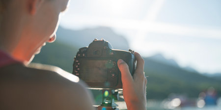 Over the shoulder view of a young female photographer taking photos with her camera on tripod  at sunrise setting up the settings and screen.の写真素材