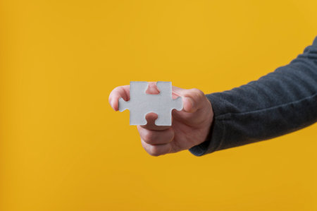 Male hand holding blank puzzle piece over bright yellow background.の写真素材