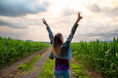 Young woman standing in the middle of green summer corn field with her arms raised high in victorious gesture. Celebrating and enjoying life and freedom.の写真素材