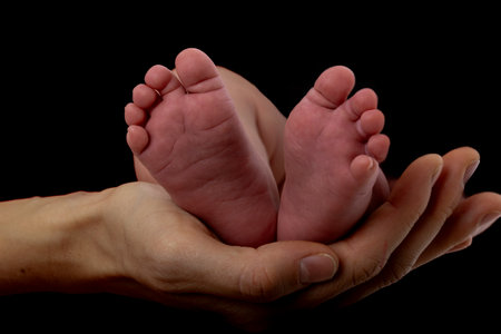 Hand of a mother holding tiny baby feet over black backgorund. Studio shot.の写真素材