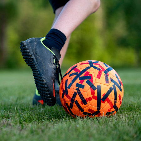 Closeup view of a teenagers foot about to kick a soccer ball on green grass in football practice.