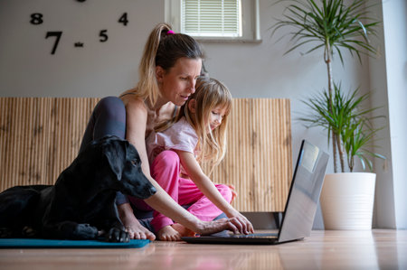 Young mother working from home using laptop computer sitting on the living room floor with her toddler daughter in her lap and teir family dog beside them.の写真素材