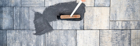 Top view of a broom brushing tile gaps sand in between cement tiles on a freshly paved patio or sidewalk.の写真素材