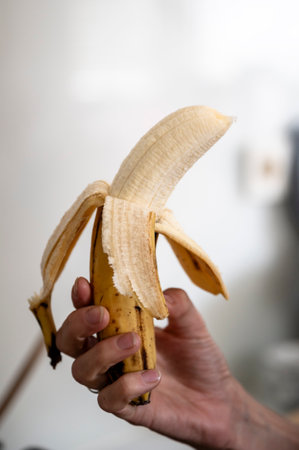 Closeup view of female hand holding a half peeled banana. Healthy snack time.の写真素材
