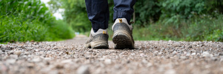 Wide view image of male legs walking on a gravel path in a journey through nature. View from below of the sole of hiking shoes.の写真素材