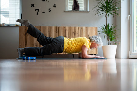 Senior man practicing pilates plank exercise with a lifted leg for strong and healthy body and for...