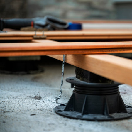 A detailed shot of wooden beams on adjustable pedestals during deck construction, secured by metal brackets. Tools rest in the background, showcasing precision and craftsmanship.の写真素材