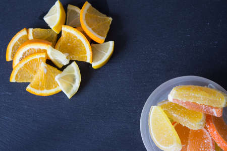 Colorful sugary marmalade. Lemon and orange slices covered with sugar in plate. Fruit jelly candies. Closeup. Top view on slate backgroundの写真素材