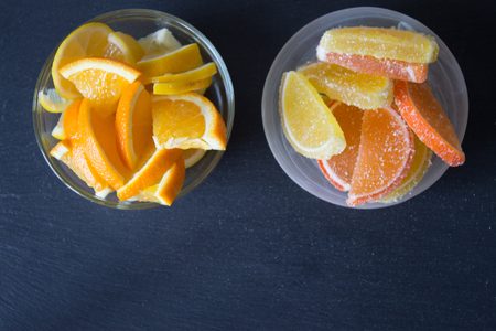 Colorful sugary marmalade. Lemon and orange slices covered with sugar in plate. Fruit jelly candies. Closeup. Top view on slate backgroundの写真素材