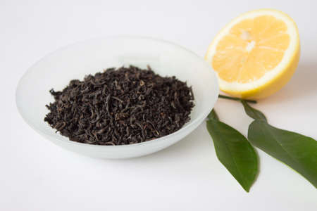 Dry tea in a beautiful bowl and lemon with green leaves on white  backgroundの写真素材