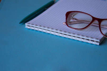 notebook and red glasses in composition on blue backgroundの写真素材