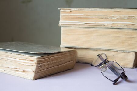 stack of old books with a pair of glasses  pink backgroundの写真素材