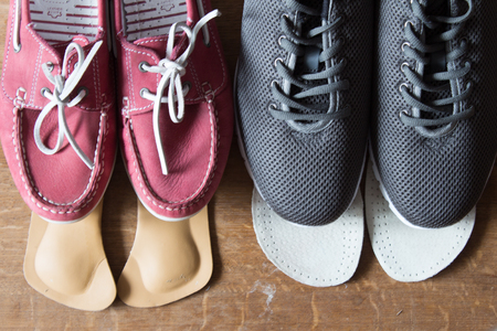 Gray sport shoes and pink sneakers with orthopedic insoles. Wooden background.の写真素材