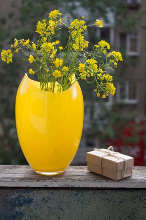 Bouquet of yellow flowers in vase. Gift box and wild flowers are location on the balcony wooden railing.の写真素材