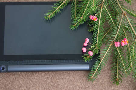 Christmas background with green spruce branches with pink decorations and tablet computer. Top view.の写真素材