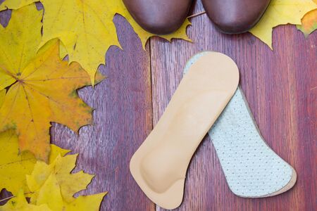Brown shoes with orthopedic insoles. Autumnal background, maple leaves on a wooden board. Top viewの写真素材