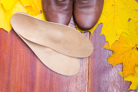 Brown shoes with orthopedic insoles. Autumnal background, maple leaves on a wooden boardの写真素材
