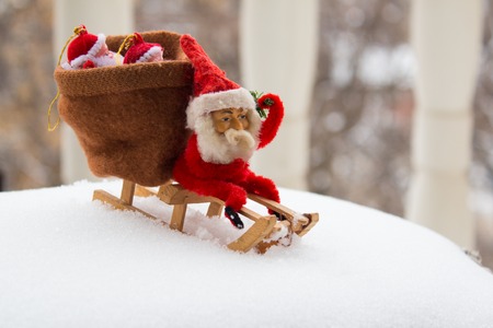 Christmas gnome sits on wooden sled with bag of gifts behind him. Real snow background. Vintage toyの写真素材