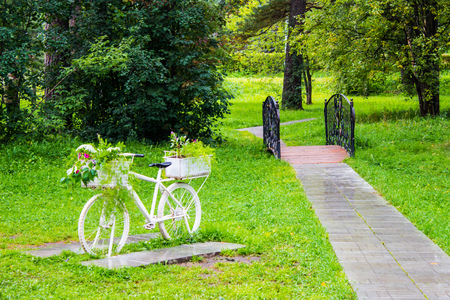 Vintage white bicycle with baskets of flowers among the garden. Beautiful decoration on natural background.の写真素材