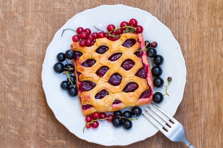 Cake with berry jam is served with fresh  red and black currant on a wooden table. Top view.の写真素材