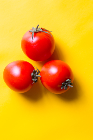 Ripe red tomatoes with green leaves isolated on yellow background. Top view.の写真素材