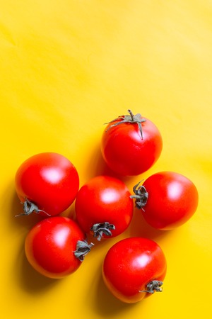 Ripe red tomatoes with green leaves isolated on yellow background. Top view.の写真素材