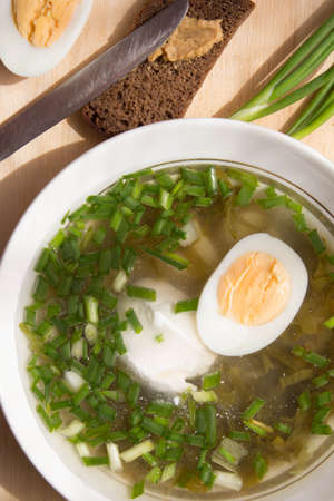 Cold vegetable soup with green onion, sorrel, boiled egg, sour cream on wooden board. Homemade refreshing dish.の写真素材
